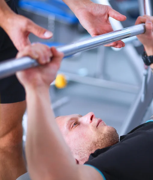 Joven levantando la barra en el gimnasio con instructor — Foto de Stock