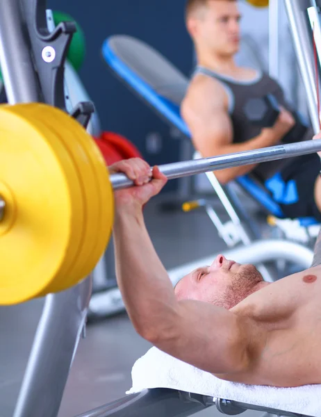 Jeune homme levant la barre dans la salle de gym avec instructeur — Photo