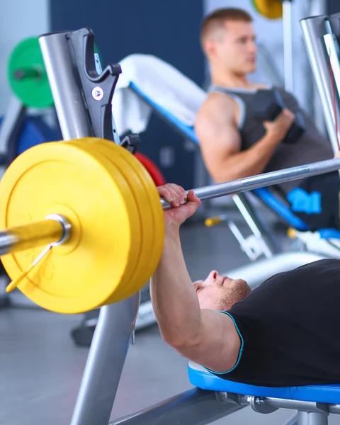 Jeune homme levant la barre dans la salle de gym avec instructeur — Photo