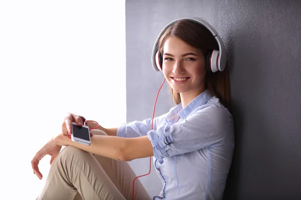 Ragazza sorridente con le cuffie seduto sul pavimento vicino al muro — Foto Stock