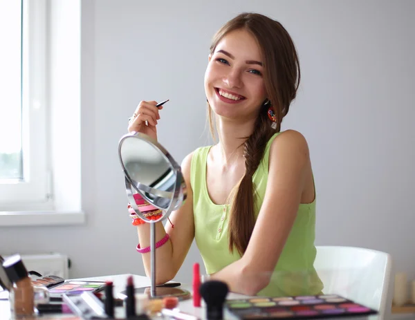 Giovane bella donna che fa il make-up vicino specchio, seduto alla scrivania — Foto Stock