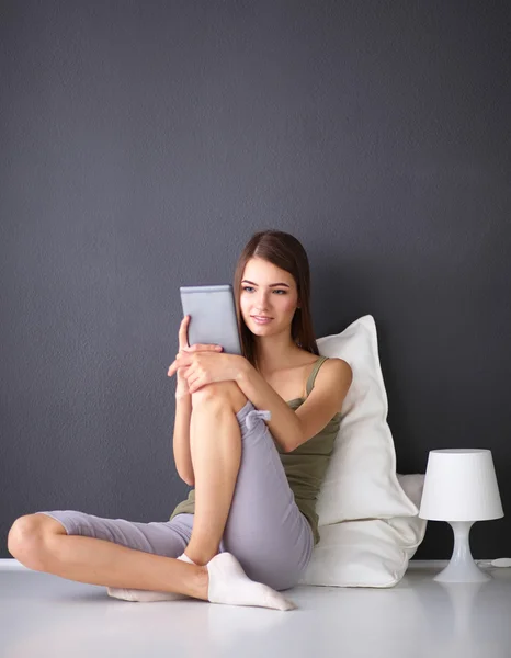 Mujer morena bonita sentada en el suelo con una almohada y mesa de avión — Foto de Stock