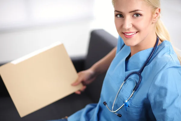 Retrato de un joven médico feliz sentado en el sofá con la carpeta — Foto de Stock