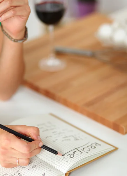 Young  woman standing in her kitchen writing on a notebook at home — Stock Photo, Image