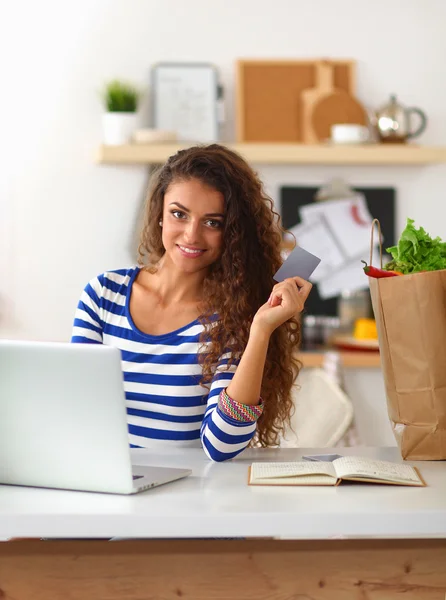 Lachende vrouw online winkelen met behulp van computer en creditcard in de keuken — Stockfoto