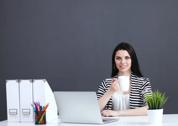 Молода жінка з ноутбуком сидить ізольовано на сірому фоні — стокове фото