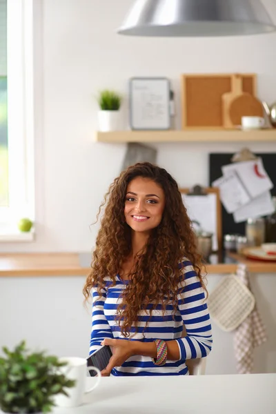 Усміхнена молода жінка з чашкою кави і ноутбуком на кухні вдома — стокове фото
