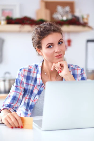 Mujer sonriente compras en línea utilizando la computadora y la tarjeta de crédito en la cocina — Foto de Stock