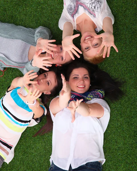 Vier jonge vrouwen liggen op groen gras met handen omhoog — Stockfoto