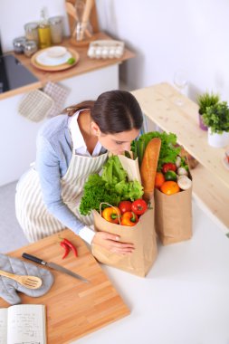 Mutfakta alışveriş torbaları olan bir kadın, masanın yanında duruyor.
