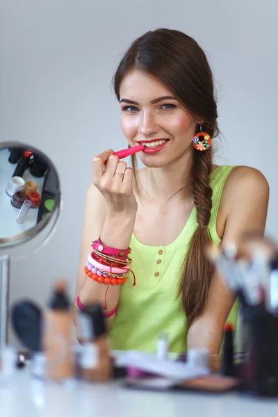 Joven hermosa mujer haciendo maquillaje cerca del espejo, sentado en el escritorio — Foto de Stock