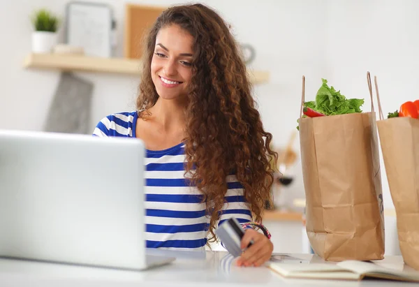 Lächelnde Frau beim Online-Shopping mit Computer und Kreditkarte in der Küche — Stockfoto