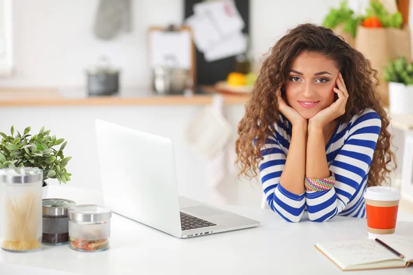 Mujer joven sonriente con taza de café y portátil en la cocina en casa — Foto de Stock