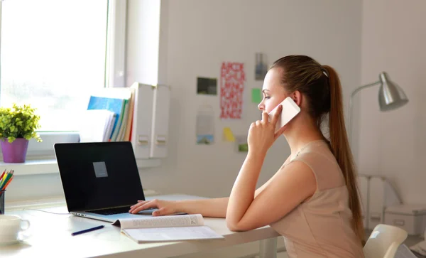 Jonge zakenvrouw zit aan het bureau en praat over de telefoon — Stockfoto