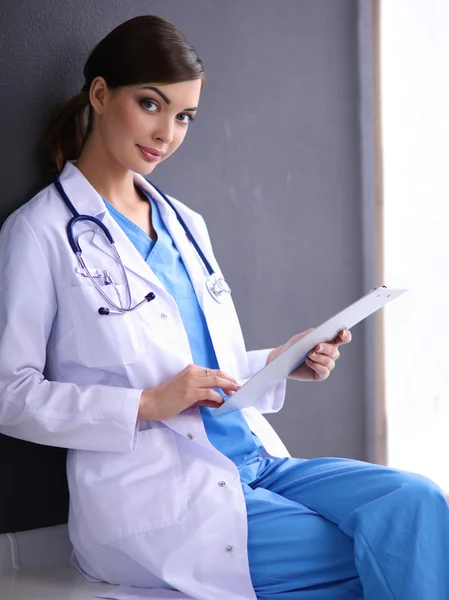 Krankenschwester hält Ordner in der Hand und macht Notizen - sitzt auf grauem Hintergrund — Stockfoto