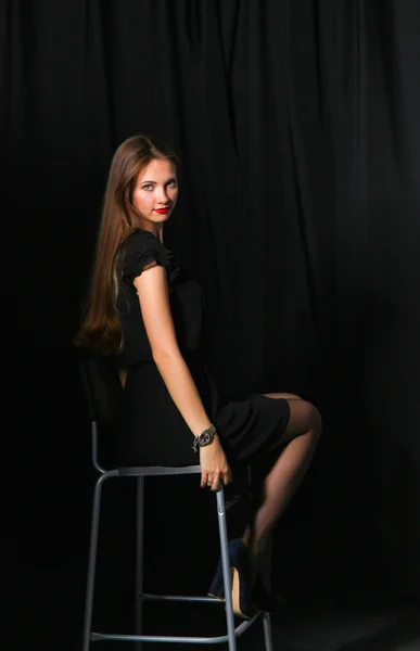 Vacker kvinna sitter en stol, isolerad på svart bakgrund — Stockfoto