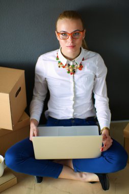 Woman sitting on the floor near a boxes  with laptop  clipart