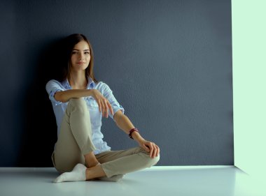 Genç bir kadın yerde, kara duvarın yanında oturuyor.