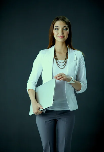 Young woman holding a laptop, standing on gray background — Stock Photo, Image