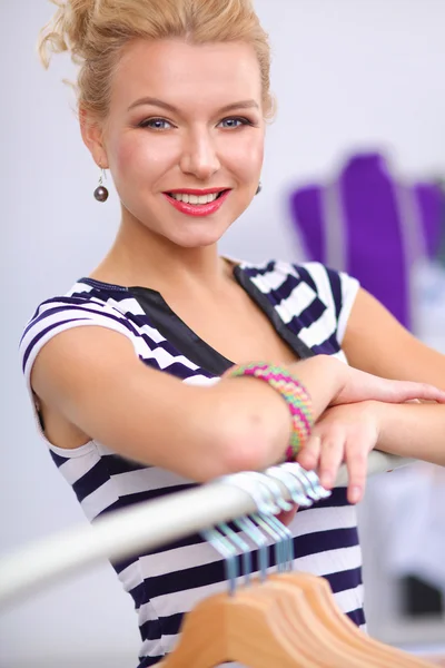 Mooie jonge stylist in de buurt van rack met hangers in office — Stockfoto