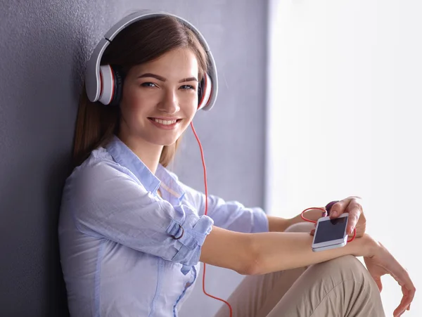Smiling girl with headphones sitting on the floor near wall — Stock Photo, Image