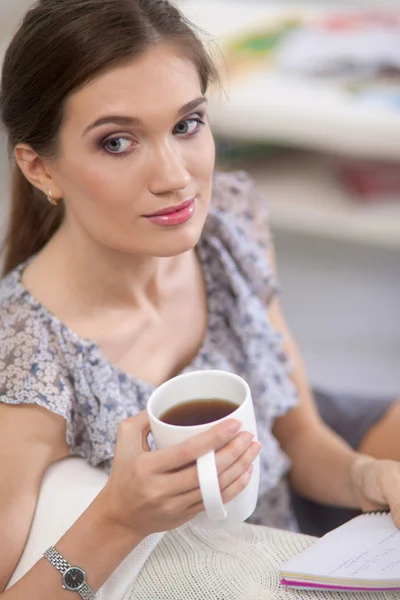 Молодая красивая женщина с чашкой на диване дома — стоковое фото