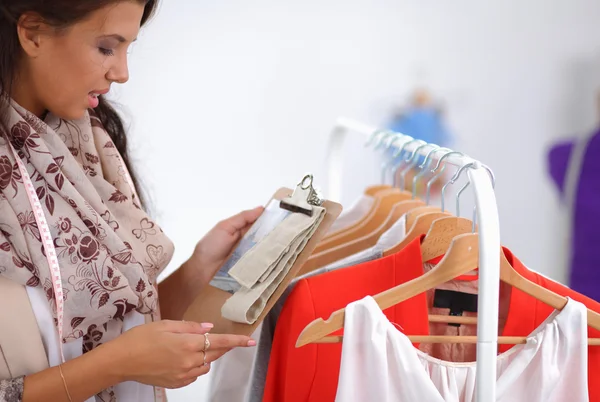 Bella giovane stilista donna vicino rack con appendini — Foto Stock