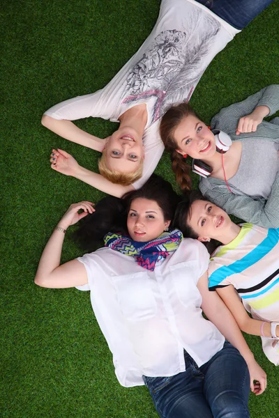 Quatro mulheres jovens deitadas na grama verde — Fotografia de Stock