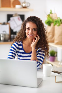 kahve fincanı ve dizüstü evde mutfakta gülümseyen genç kadın