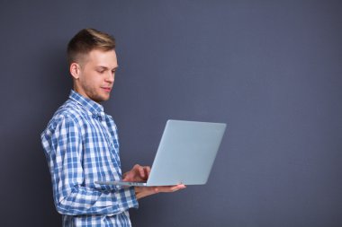 Gri arka plan üzerinde dizüstü bilgisayar konumu olan kendine güvenen genç adam portresi
