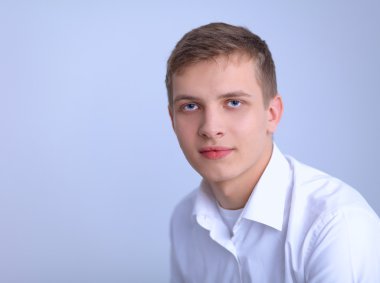 Gri arka plan üzerinde oturan gülümseyen genç adam portresi