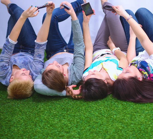 Čtyři mladé ženy leží na zelené trávě s mobilním telefonem — Stock fotografie