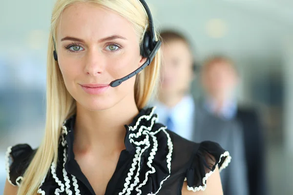 Businesswoman with headset smiling at camera in call center. Businessmen in headsets on background