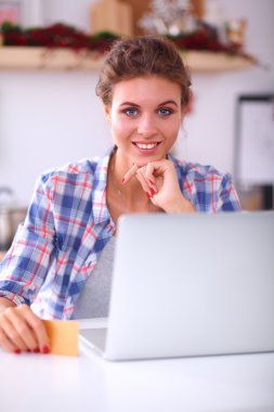 Mutfakta bilgisayar ve kredi kartı kullanan gülümseyen bir kadın.