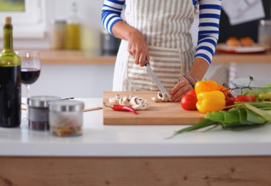 Mutfakta sebze doğrayan, masanın yanında duran genç bir kadın.