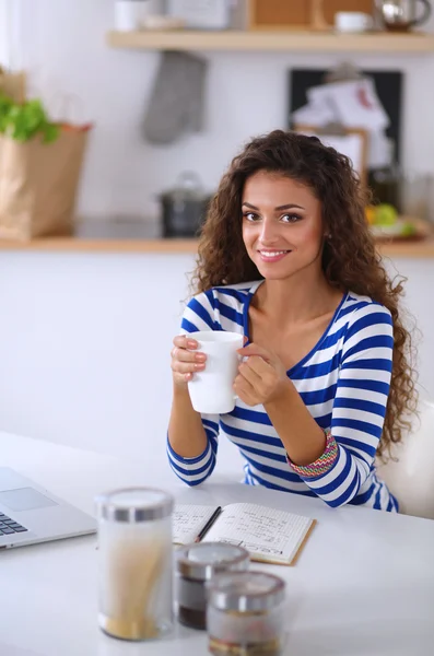 Lachende jonge vrouw met koffiekopje en laptop in de keuken thuis — Stockfoto