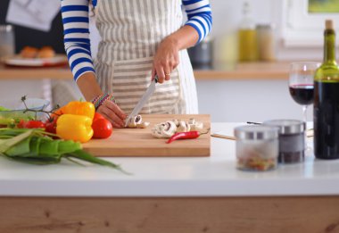 Young woman cutting vegetables in kitchen, standing near desk clipart