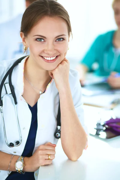 Bonito jovem sorridente médico feminino sentado na mesa — Fotografia de Stock