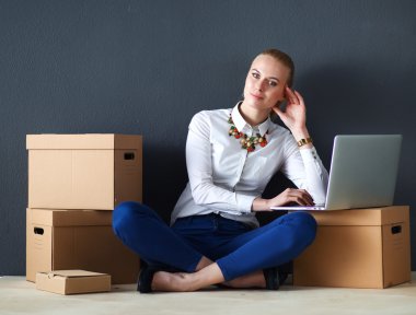 Kadın yerde dizüstü bilgisayarlı bir kutunun yanında oturuyor. 