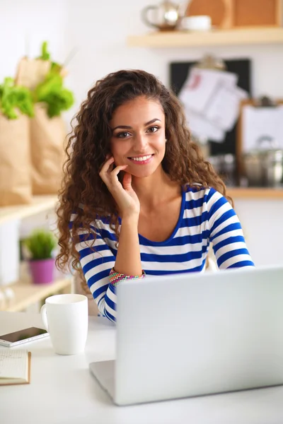 Mujer joven sonriente con taza de café y portátil en la cocina en casa — Foto de Stock