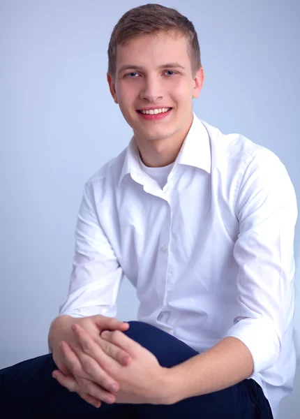 Porträtt av ung man leende sitter på grå bakgrund — Stockfoto