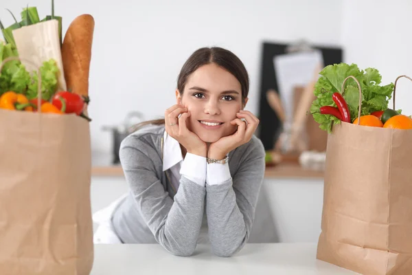 Ung kvinna som håller i matkassen med grönsaker Står i köket — Stockfoto