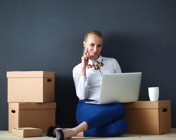 Женщина сидит на полу рядом с коробками с ноутбуком — стоковое фото