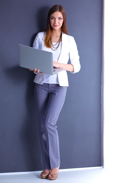 Young woman holding a laptop, standing on gray background — Stock Photo, Image