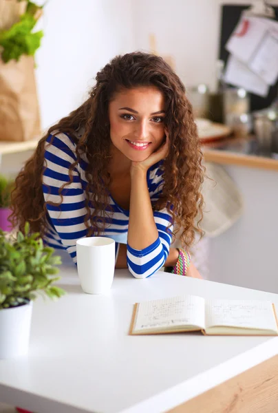 Lachende jonge vrouw met een koffiekopje in de keuken thuis — Stockfoto