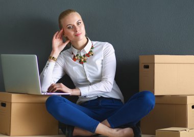 Kadın yerde dizüstü bilgisayarlı bir kutunun yanında oturuyor. 