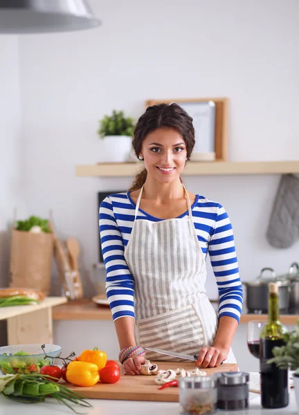 Młoda kobieta krojąca warzywa w kuchni, stojąca przy biurku — Zdjęcie stockowe