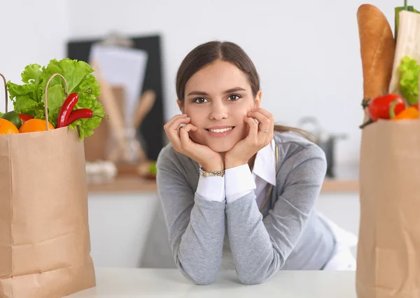 Mujer joven sosteniendo bolsa de la compra de comestibles con verduras de pie en la cocina — Foto de Stock