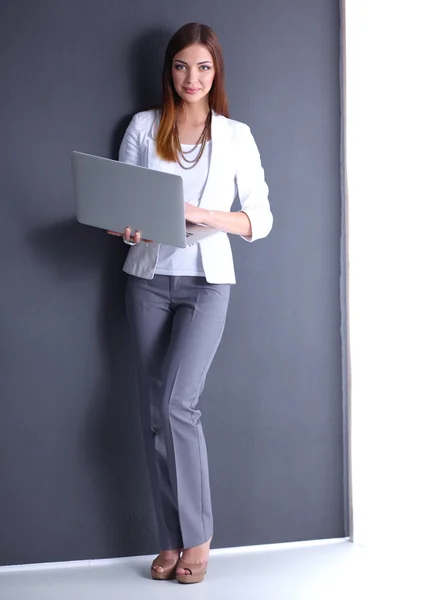 Young woman holding a laptop, standing on gray background — Stock Photo, Image