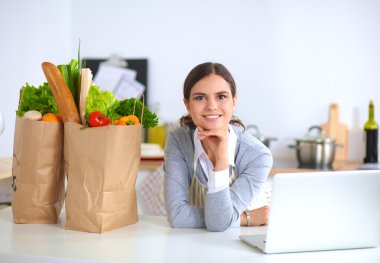 Güzel genç bayan yemek pişiriyor. Mutfakta makbuzu olan dizüstü bilgisayara bakıyor.